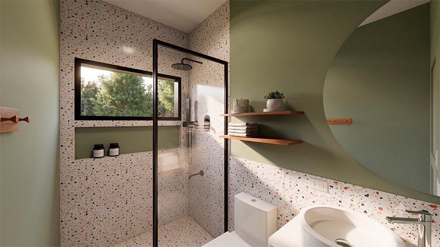 Baño pequeño con ducha de vidrio, piso terrazo y repisas de madera flotantes sobre pared verde olivo